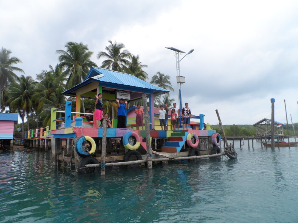 colorful little house on a raised pier with local people waving