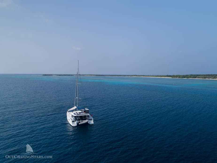 a catamaran anchored in rich blue water with a tropical atoll in the distance surrounded by turquoise waters
