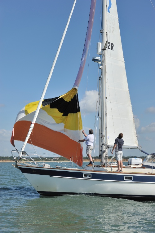 Yacht with two men on deck bring the spinnaker down.