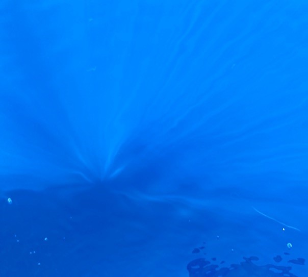 iridescent blue water with a shock of light dispersing within it and a vague shadow of the photographer reflected