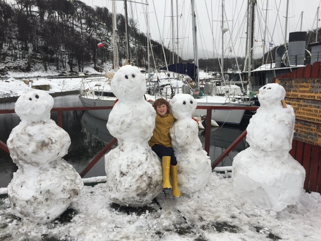 Child posing with 4 snowmen with boats in the background